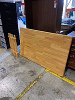 Butcher block wooden table top leaning against furniture, showing the surface and some scuffing on edges with four wooden table legs nearby.