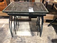 Close view of the three tables nested inside each other, showing metal mesh tops and legs.
