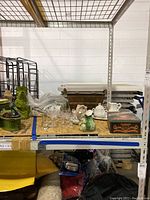 Photo showing entire lot on shelving including glassware, teacups, candle holders, pitcher, and branded tins and basket