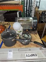 Photo showing Hamilton Beach toaster oven, Circulon pot with lid, Anolon saucepan, two planters with fruit design and a light bulb on a wooden surface.