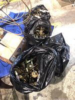 Four black plastic bags filled with brass wall sconces and parts, some light bulb sockets and candle-shaped bulbs visible.