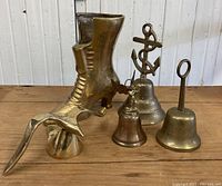 Five vintage brass figures including a boot and four handbells with different handles arranged on wooden surface.
