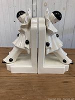 Side view of pair of ceramic clown bookends showing symmetrical design, glossy white finish with black accent details