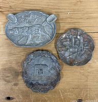 Top view of all three metal vintage ashtrays arranged on a wooden surface showing their embossed designs.