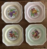 Top-down image showing all four plates with different fruit designs and varied pastel backgrounds, each plate approx 7.5 inches wide.