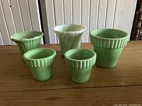 Five vintage green and white Akro Agate flower pots arranged on wooden table, showing ribbed and fluted designs.