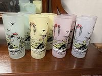 Set of eight tall vintage drinking glasses in three tint colors with dancing woman, bird, and trellis designs.