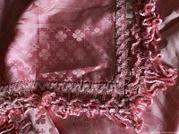 Close-up of the edge showing the textured pink ruffled trim and damask floral pattern on pink satin fabric.