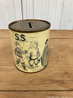Front and side views of a cylindrical vintage tin coin bank with illustrations of children in missionary aid costumes, made in Toronto.
