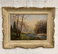 Framed landscape oil painting showing overall view with cream textured vintage frame and classic rural scene with trees and river.