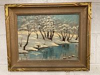 Full view of the framed painting showing winter snow scene with a river and trees in a gold frame.