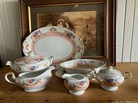 Nine pieces of vintage Harmony House china with Grandeur pattern shown on wood surface with framed sepia photo in background.