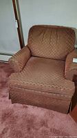 Front view of brown Norwalk upholstered arm chair with pleated back cushion and skirted base on carpeted floor.