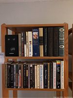 Wooden bookshelf filled with various hardcover and softcover books on history, politics, and literature, along with a compact speaker.