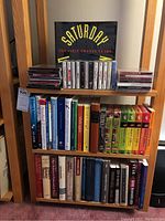 Two wooden shelves filled with books on therapy topics, stacked CDs and cassettes, and a boxed DVD set of Saturday Night Live's first 25 years.
