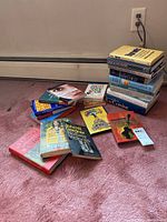 Stack of various books on carpeted floor near baseboard heater and electrical outlet
