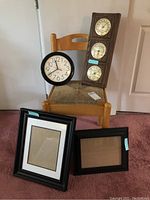 Lot as a group: wood chair with rush seat, wall clock, vertical barometer, and two black picture frames with matting on the floor.