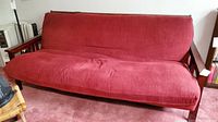Front view of the futon couch with red fabric cushion and wooden frame showing wear and shape.