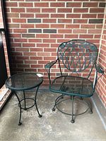 Metal patio swivel chair and matching round metal side table on concrete floor against brick wall.