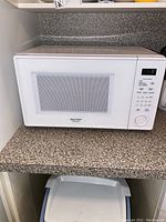 Front view of the Sharp microwave on a kitchen counter showing overall design, with a white door and window, and control panel on the right side.