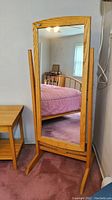 Full view of the upright standing swivel mirror with wooden frame in a bedroom setting showing its height and base.