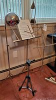 Full view of music stands with sheet music, chrome adjustable ball lamp, and tripod on floor against window.