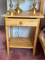 Side view of one wooden nightstand showing drawer partially open and slatted lower shelf, with two brass lamps on top.
