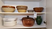 Photo showing four pottery bowls on top shelf and white Corning Vision Ware dishes, amber casserole, and green pitcher on bottom shelf