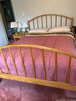 Front view of the queen bed frame showing curved headboard and footboard with vertical slats and natural wood finish.