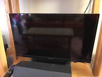 Front view of Sharp 24 inch LCD smart TV on wooden shelf, black bezel and screen turned off.