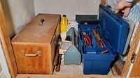 Photo showing wooden toolbox, blue and green plastic toolboxes with various hand tools, pliers and screwdrivers visible, placed in storage closet.
