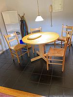 Wide view of round wooden dining table with four ladder back chairs and placemats on top