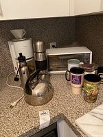 Shows the Black and Decker toaster oven, Krups coffee maker, coffee grinder, kettle, and beverage containers on a kitchen countertop.