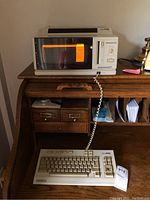 Photo showing the main vintage Magnavox Videowriter 350 unit on a desk with its connected keyboard in front. The screen is illuminated with an orange glow.