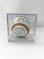 Photo of the blue ink signed white official American League baseball in a clear acrylic display case, showing multiple signatures, including Bobby Ramos and Joe Mota.
