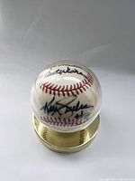 Side angle showing Kelly Gruber's signature and part of the inscription on the baseball inside a clear display case with gold base.