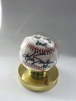 Front view of the signed baseball inside the clear display case mounted on a gold-tone base, showing the signature and inscription.