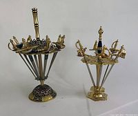 Two mini sword holders with brass and black handles and swords arranged around decorative bronze bases