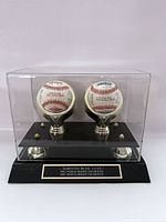 Two official world series baseballs displayed in a clear acrylic case with black base and metal stands