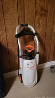 Front view of the 3 gallon plastic sprayer on wheels with wrapped handle and orange cap.