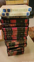 Stack of 20 black hardbound Collier's Year Books with red and gold labels, 2 volumes of The New Book of Knowledge with blue and white covers, and National Geographic Index book on top