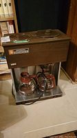 Front of Brewmatic Diplomat 11 coffee maker showing main machine with dual warming plates, control switches, and two glass carafes below.