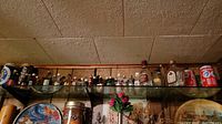 Shelf with multiple empty liquor bottles and collectible cans including Toronto Blue Jays commemorative Coca-Cola cans.