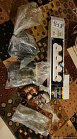 Photo of enclosed Hampton Bay bath bar 4-light fixture box displayed with plastic bags containing plumbing parts on carpet.