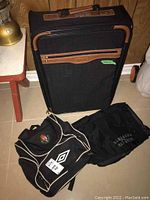 Front and angled view of one upright luggage suitcase with brown trim and two black carry bags placed on floor.