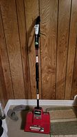 Full view of the Noma Turboshovel snow shovel standing vertically against a wood-paneled wall, showing overall condition and length.