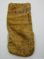 Full length view of soft fabric pocket pouch with embroidered and beaded text 'Gladys 1903 40 Mile Yukon'. Shows discoloration and wear on the fabric.