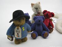 Group photo showing the H.C.F miniature Paddington bear, three small miniature bears in purple and red, one miniature cat, and four felt ornaments in the background.