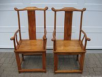 Front view of two antique Chinese yoke back "Official's Hat" chairs showing the curved crest rail, vertical back slats, wooden seat and armrests.