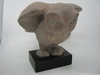 Front view of owl sculpture showing facial features and wings raised in prodding position.